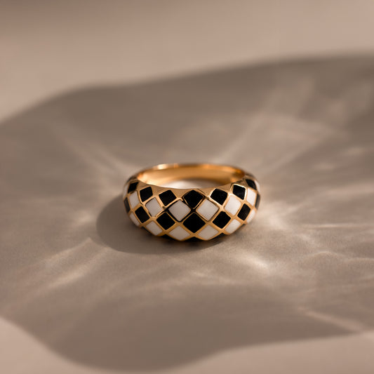 Gold dome ring with black and white checkered enamel pattern, displayed on a neutral surface.