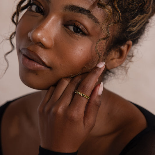 Close-up of a person wearing a gold ring with green peridot marquise cut stones on a neutral background