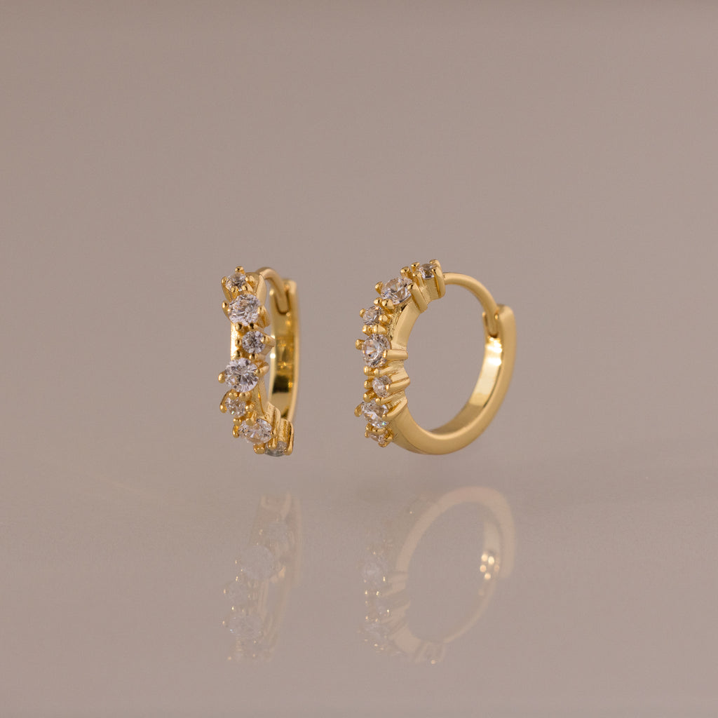 Marquise Cluster Hoop Earrings in gold with clustered CZ diamond stones, shown standing on a soft neutral surface.