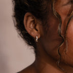 A close-up of a woman's ear showcases the Diamond Cluster Hoops in 18K Gold—elegant small gold hoops adorned with sparkling round cut stones for a dazzling effect.