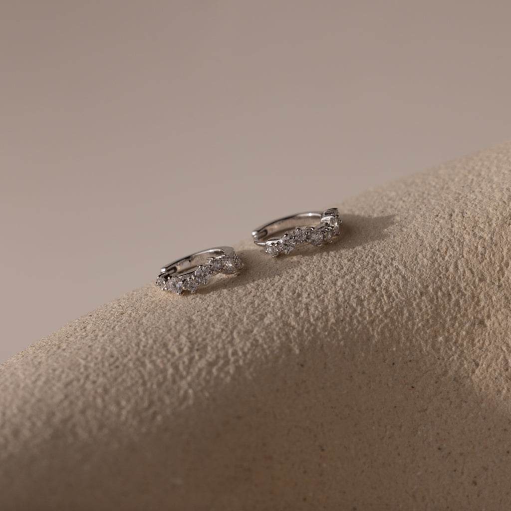 Marquise Cluster Hoop Earrings in silver with clustered CZ diamond stones, resting on a neutral surface.