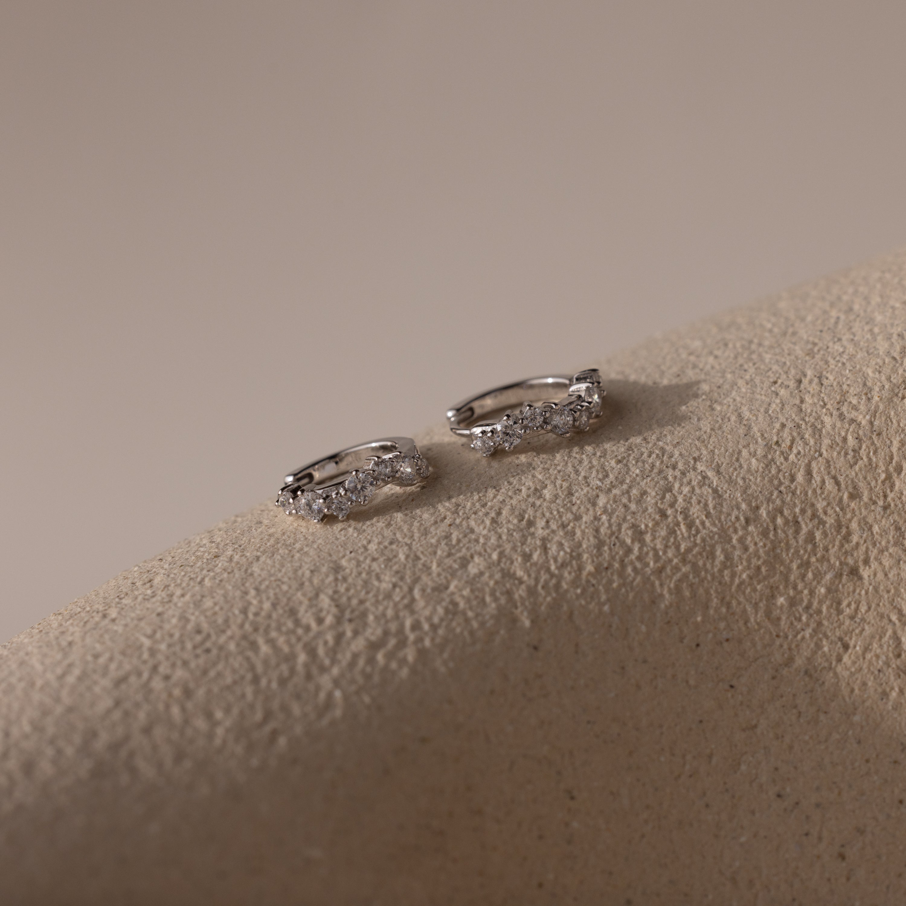 Marquise Cluster Hoop Earrings in silver with clustered CZ diamond stones, resting on a neutral surface.