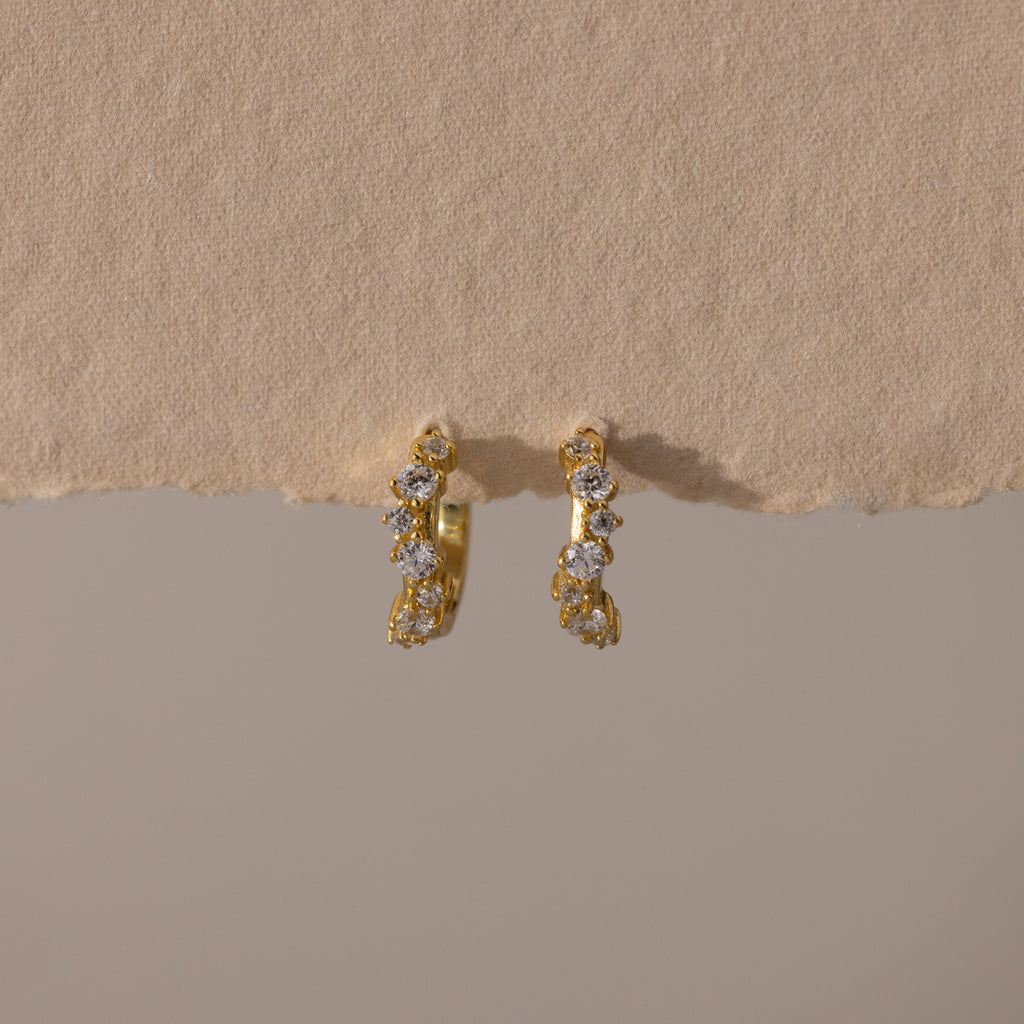 Marquise Cluster Hoop Earrings in gold with clustered CZ diamond stones, displayed on a soft neutral surface.