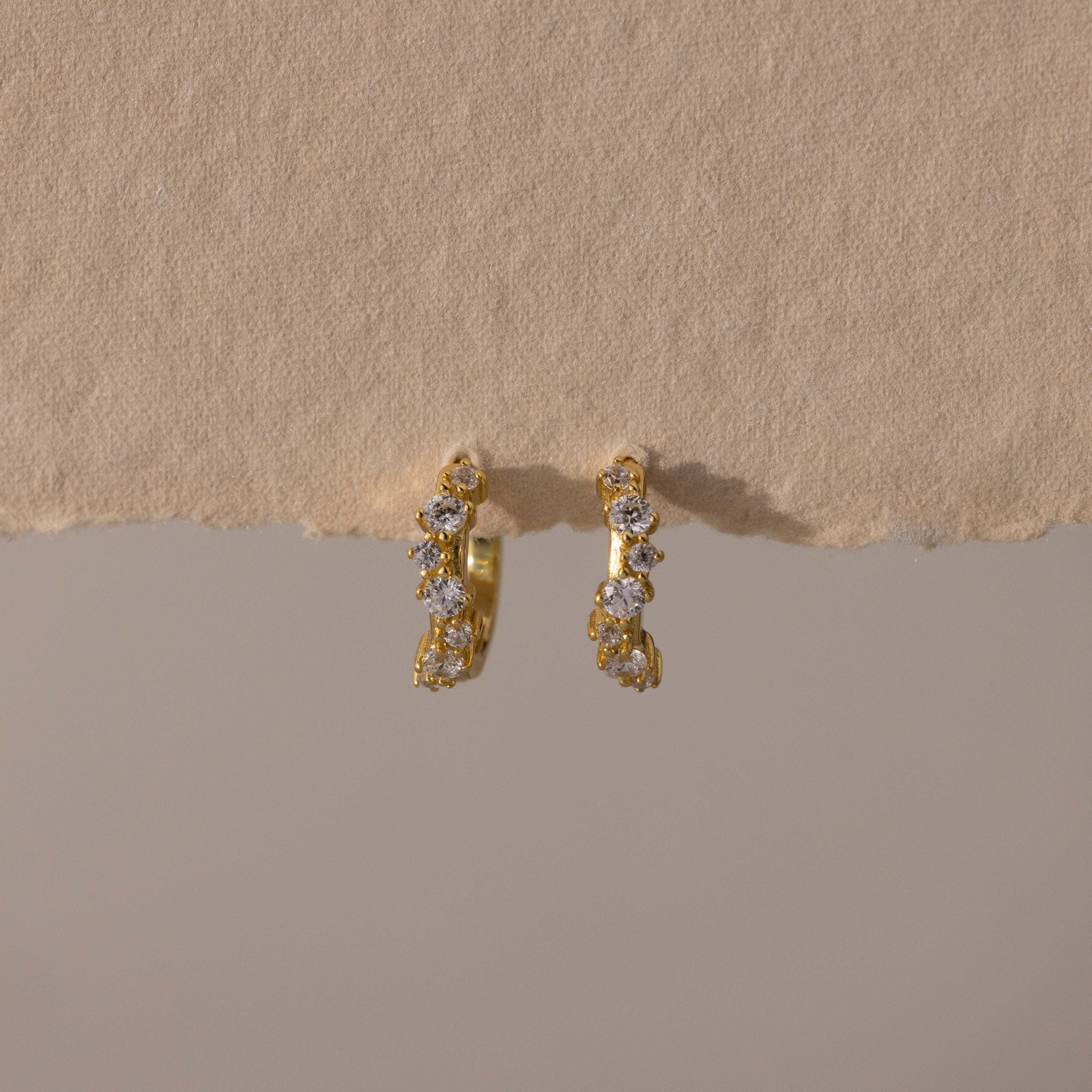 Marquise Cluster Hoop Earrings in gold with clustered CZ diamond stones, displayed on a soft neutral surface.
