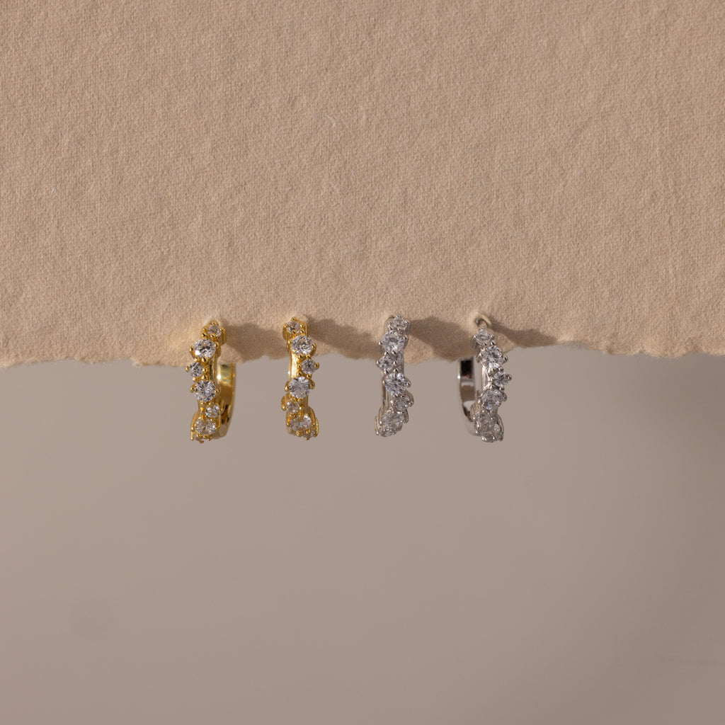 Two pairs of Marquise Cluster Hoop Earrings in gold and silver with clustered CZ diamond stones, displayed on a neutral surface.