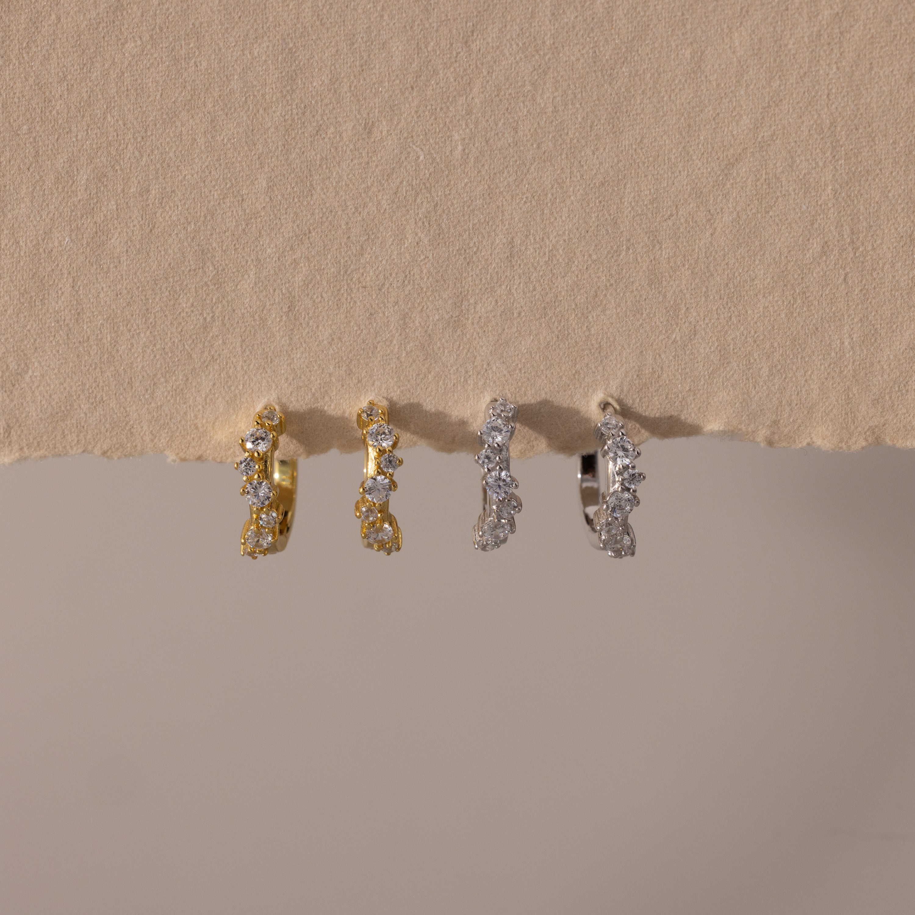 Two pairs of Marquise Cluster Hoop Earrings in gold and silver with clustered CZ diamond stones, displayed on a neutral surface.