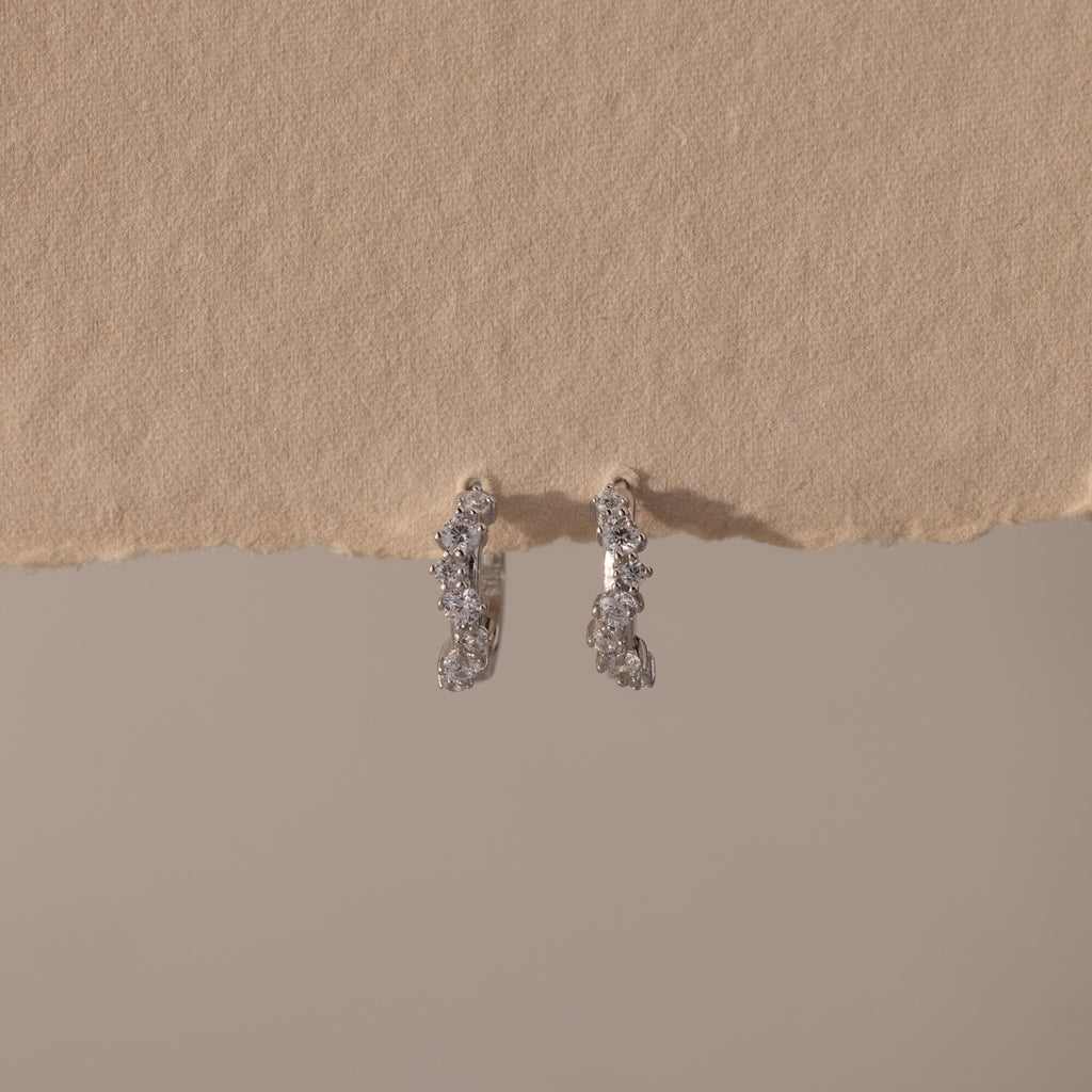 Marquise Cluster Hoop Earrings in silver with clustered CZ diamond stones, displayed on a neutral surface.