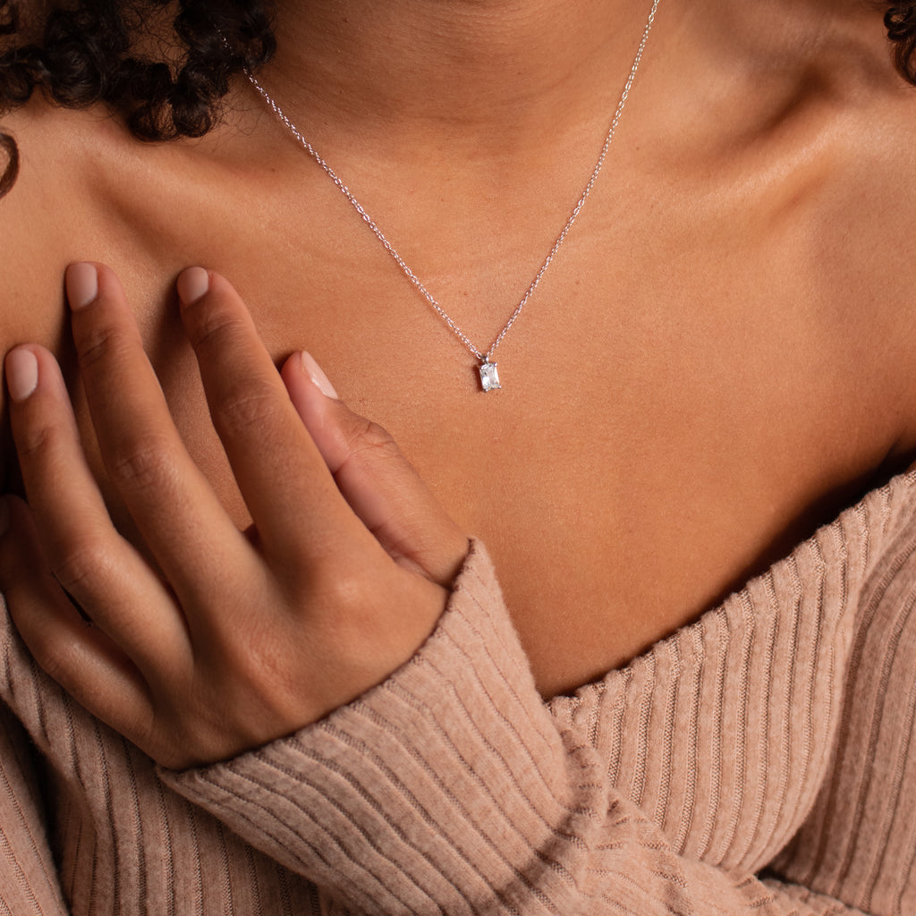 Woman wears a ribbed beige off-shoulder sweater and the Sage Diamond Necklace in Silver, showcasing timeless elegance with its rectangular pendant.