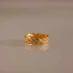 The Woven Ring features a gold braided silhouette and intricate woven design, showcased on a reflective, neutral surface.
