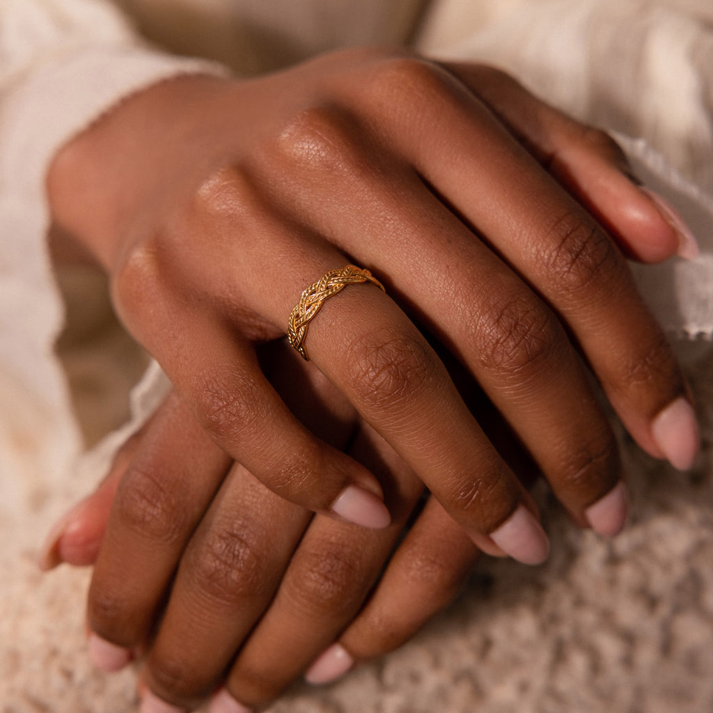 Close-up of a hand wearing the Woven Ring, a delicate gold band with a braided silhouette, resting gently on another hand.
