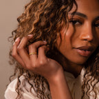 A woman with curly hair wears the Woven Ring and an off-white blouse, looking thoughtfully at the camera.