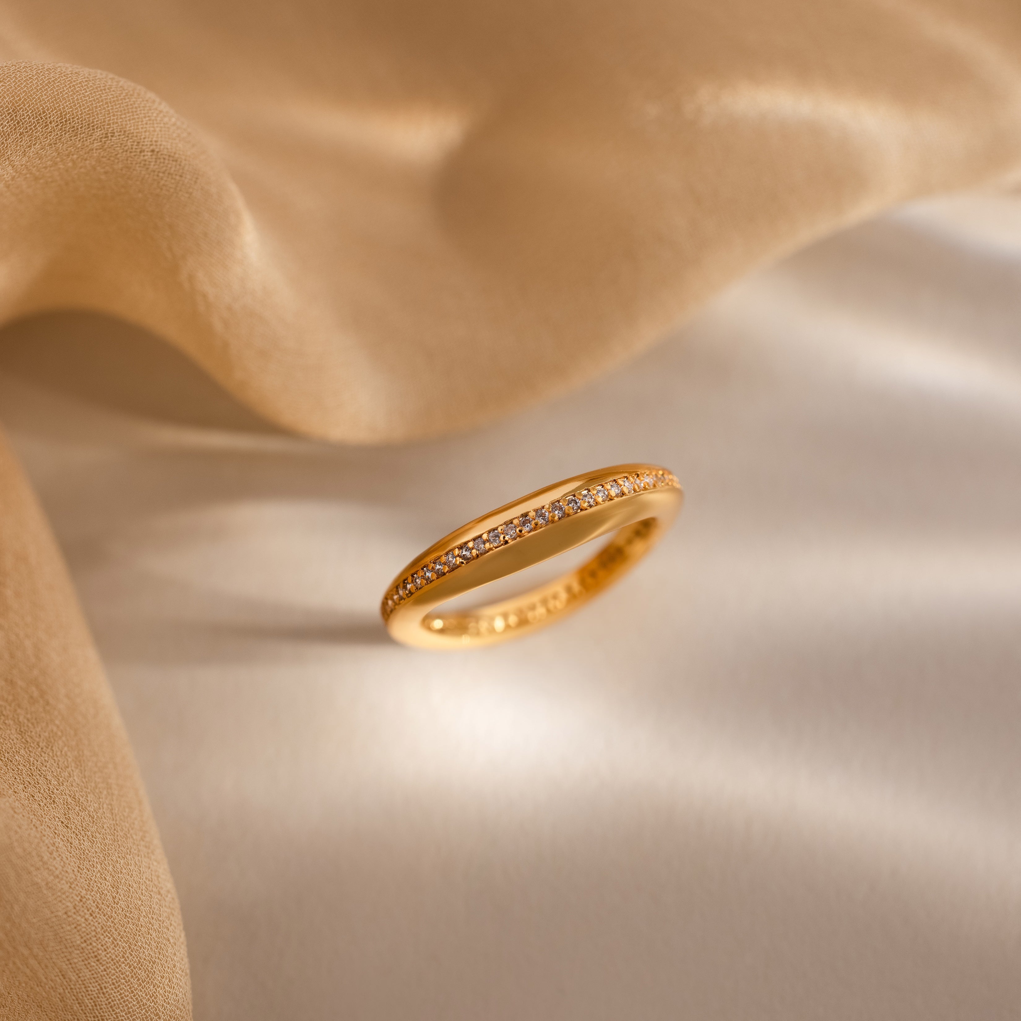 The Pave Curve Dome Ring, featuring a row of sparkling pavé diamonds, rests on soft beige fabric in gentle light—an ideal domed ring to elevate your everyday stack.