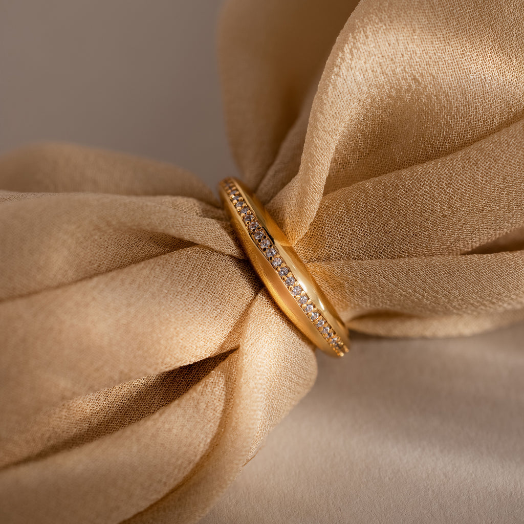 The Pave Curve Dome Ring with small diamonds rests on soft, beige fabric tied in a bow—an elegant piece perfect for your everyday jewelry stack.