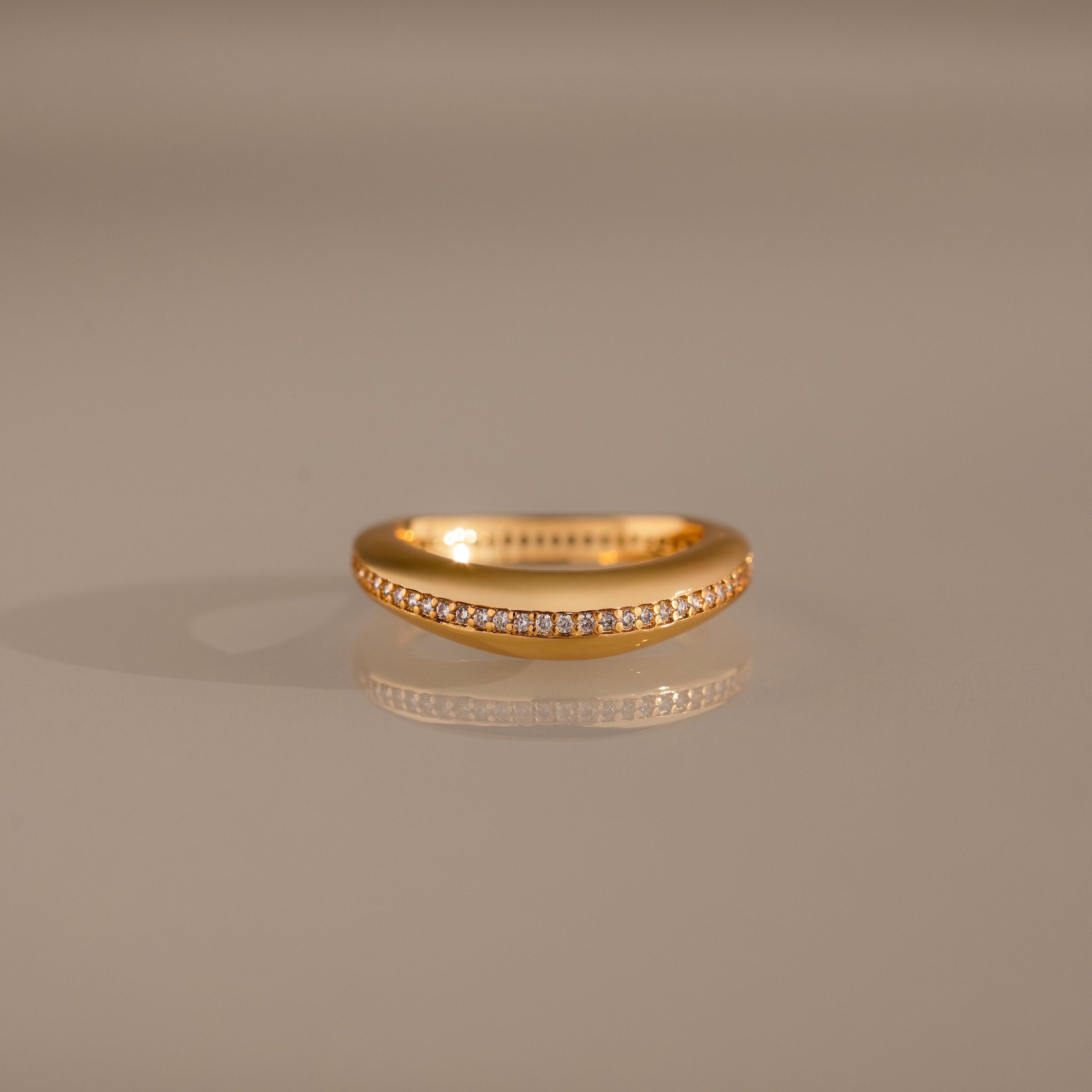The Pave Curve Dome Ring, crafted in gold and set with a row of small diamonds, is displayed on a neutral reflective surface—an ideal choice for your everyday stack.