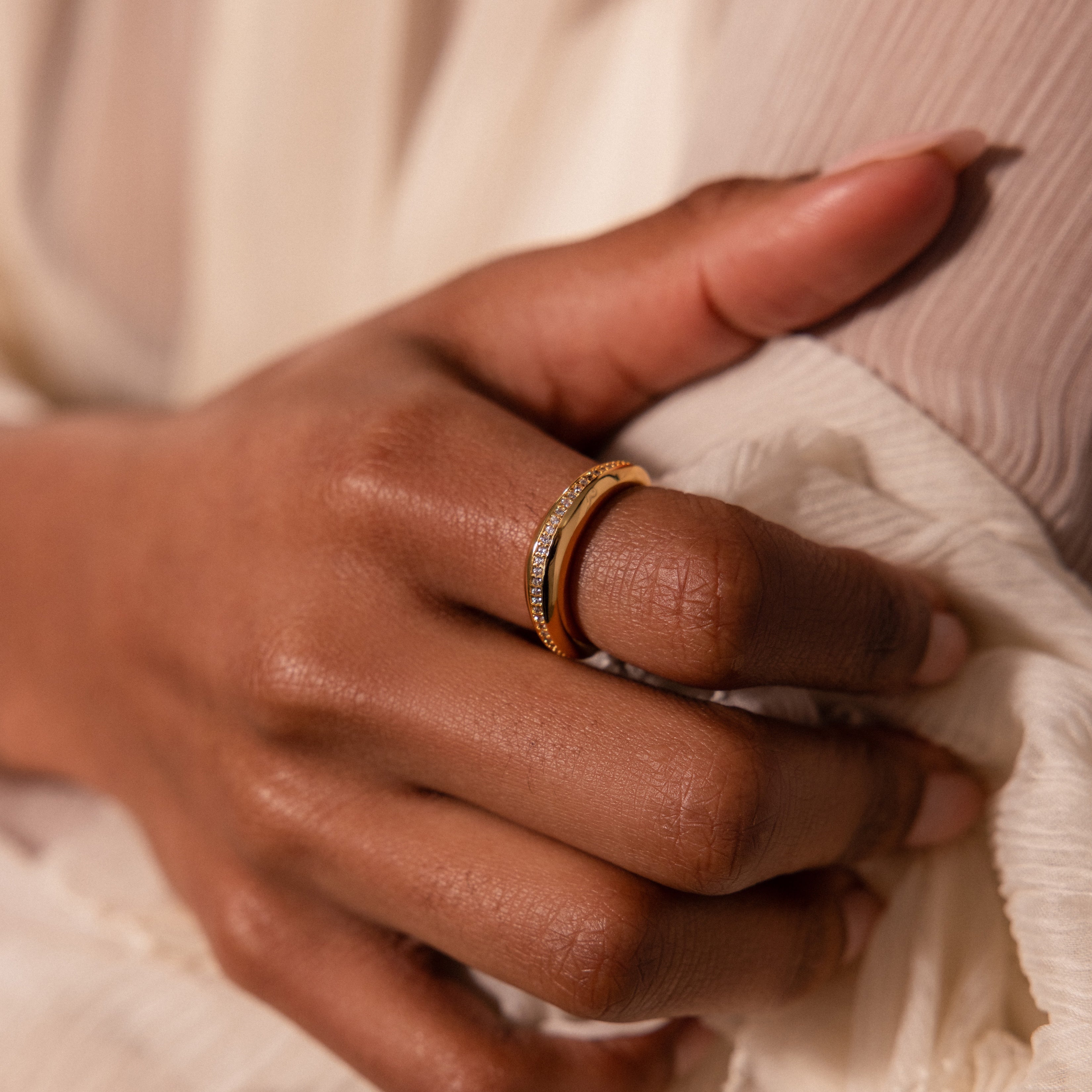 A hand adorned with an everyday stack of gold and diamond rings, including the Pavé Curve Dome Ring, gently rests on a cream-colored, textured fabric.