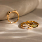 Three Baguette Signet Rings with rectangular gemstones create a modern look, elegantly displayed on a soft beige fabric background.
