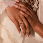 A hand with pale pink nails wears the Diamond Baguette Signet Ring, featuring a rectangular stone, resting elegantly on cream fabric.
