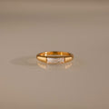 Diamond Baguette Signet Ring: This modern gold ring features a rectangular diamond centerpiece, showcased on a reflective beige surface.