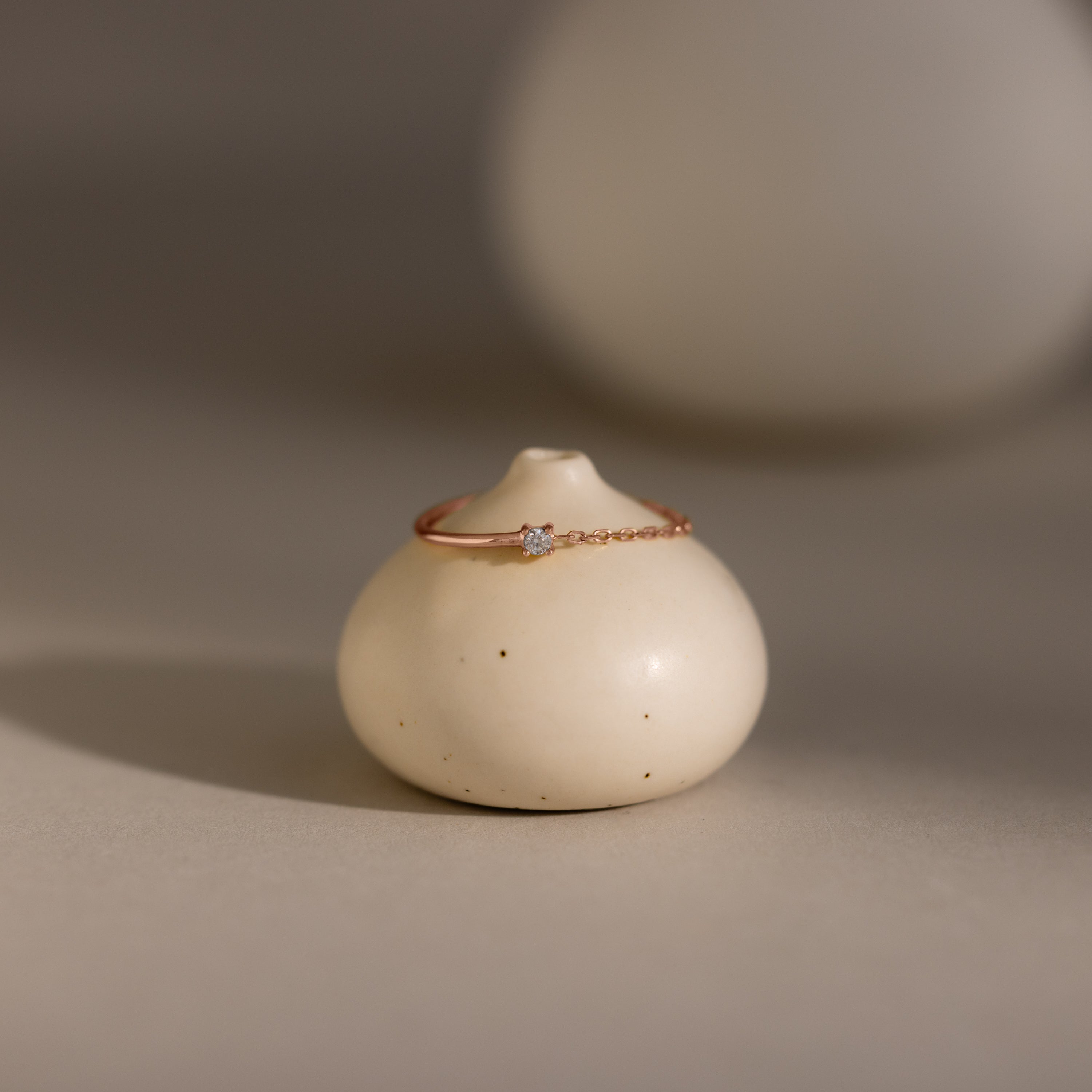 The Diamond Half Chain Ring, featuring a delicate gold design with a small diamond, rests on a round white ceramic holder—ideal for fans of dainty jewelry.