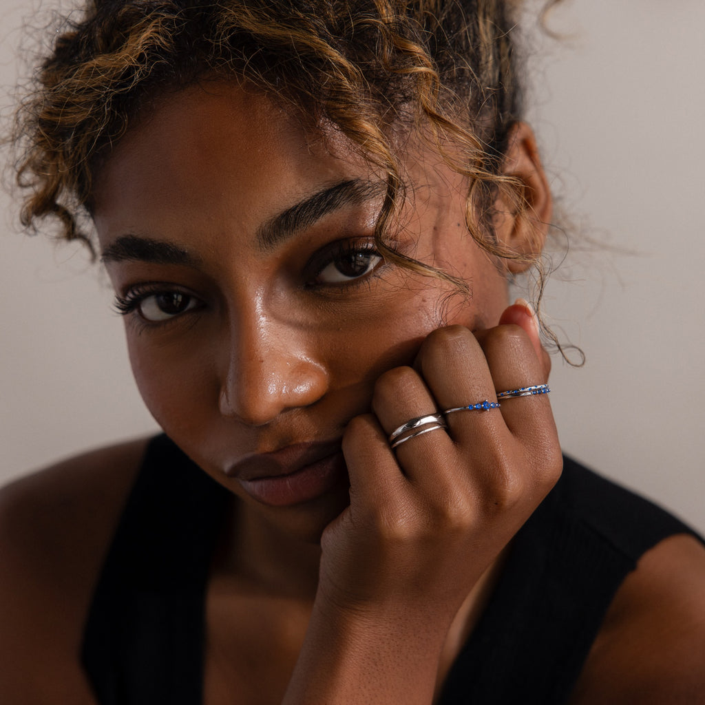 Woman with curly hair wearing multiple silver rings on a neutral background