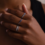 Close-up of a model wearing three rings with blue stones and a set of 2 other duo form silver rings on a dark background