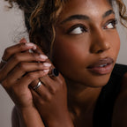 Woman with curly hair looks up, wearing the Midnight Hour Onyx Ring in Silver with an adjustable band, dressed in black, hands near her face.
