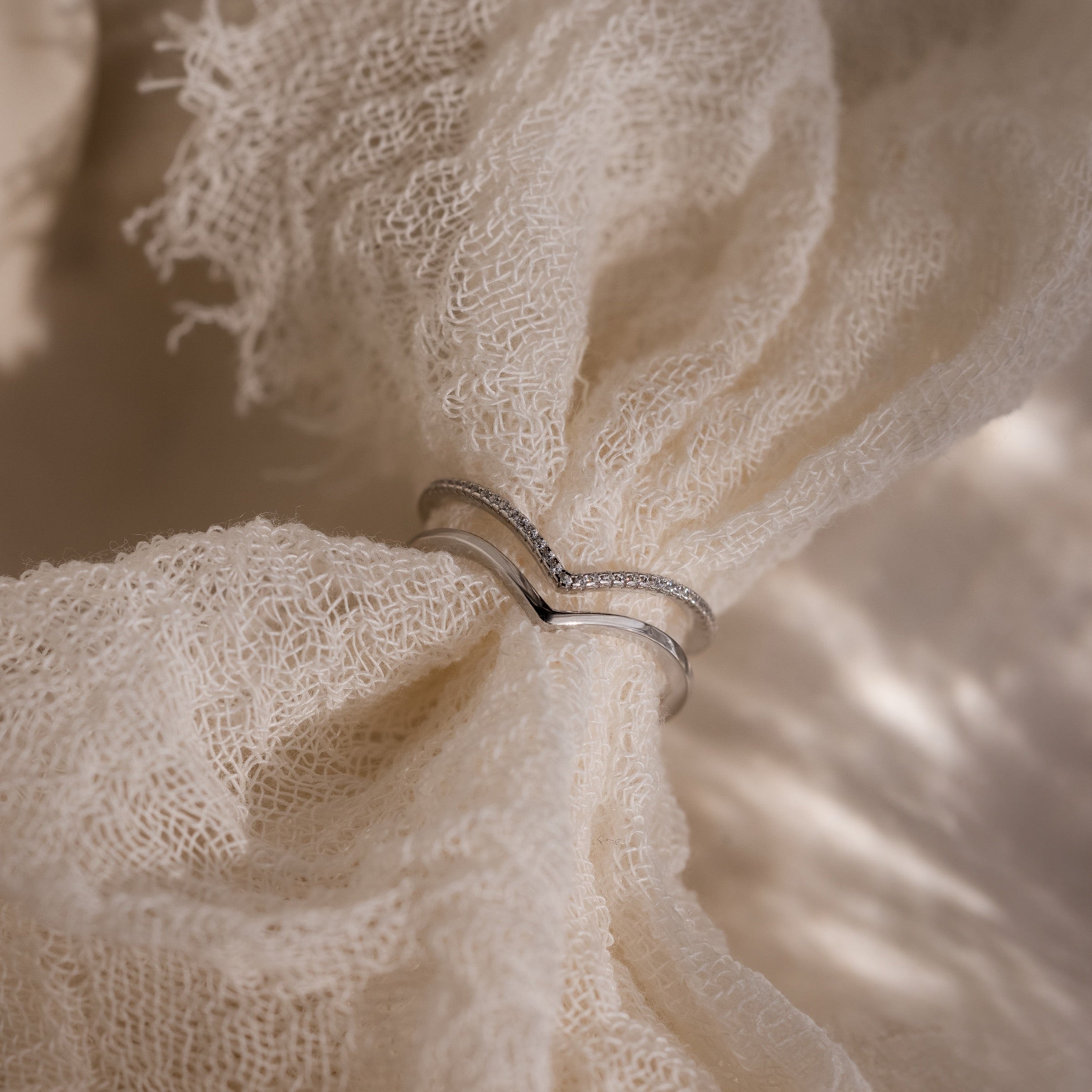 The Curve Stacking Set in Silver features two delicate rings with small diamonds forming a graceful curve, shown on textured cream fabric in soft, natural light.