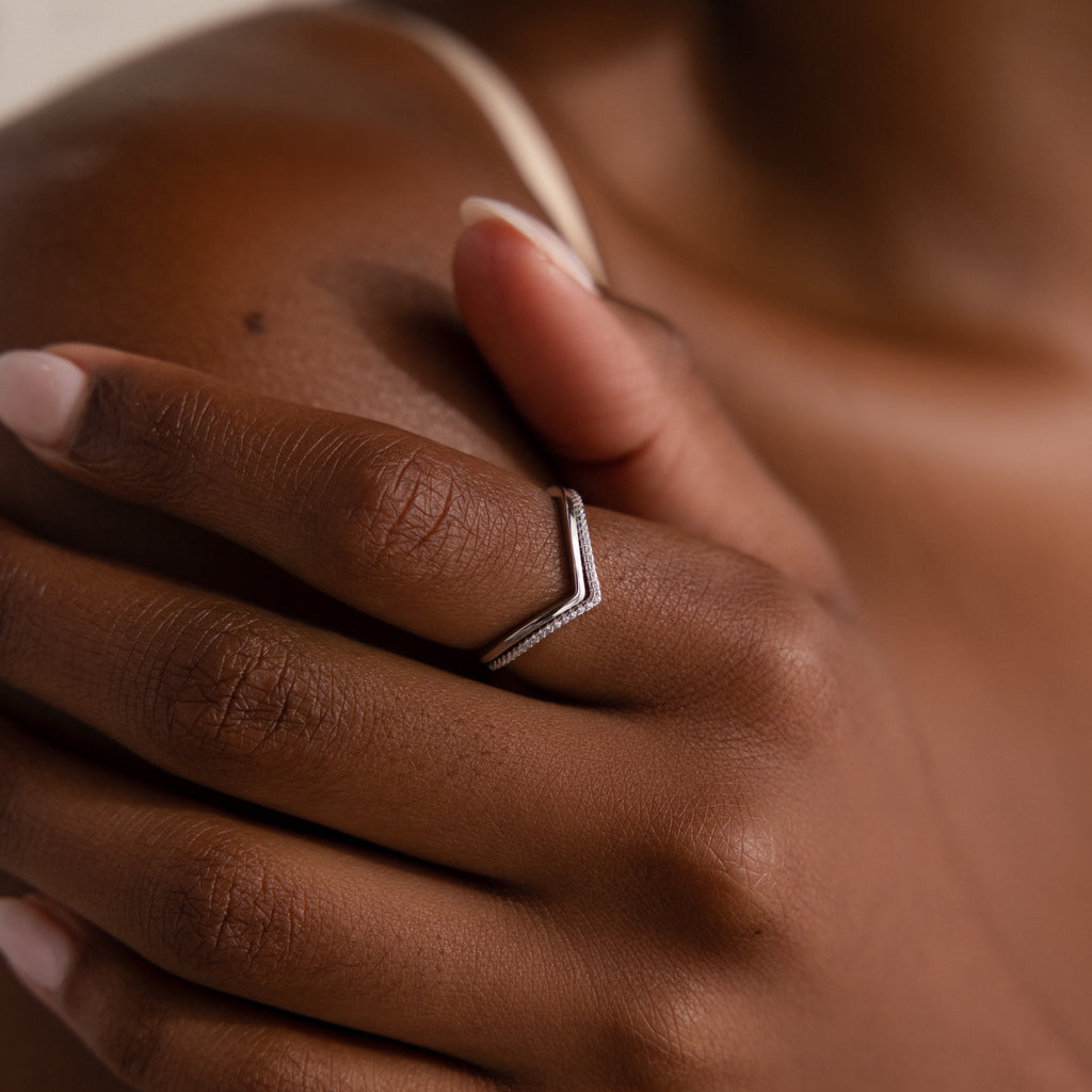 Close-up of a hand wearing the Curve Stacking Set—a silver chevron ring with thin bands—on the middle finger, gently touching the shoulder in a chic stack.