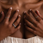 Close-up of manicured hands wearing the Curve Stacking Set in Silver, featuring thin silver bands, resting on the chest above a cream dress.