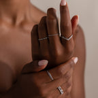 A close-up of dark-skinned hands wearing the Curve Stacking Set, featuring delicate silver thin bands stacked on several fingers.