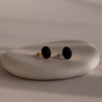 Two Midnight Hour Onyx Rings in Silver and Gold, each with a unique adjustable band, are elegantly displayed on a smooth, light-colored oval stone.