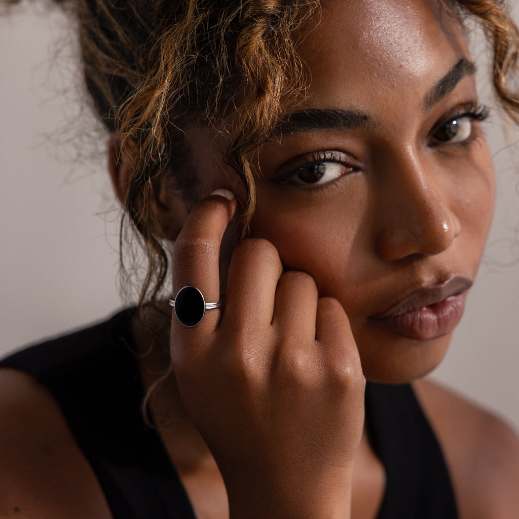 Woman with curly hair wearing a black top and the Midnight Hour Onyx Ring in Silver with an adjustable band, gazing softly at the camera.