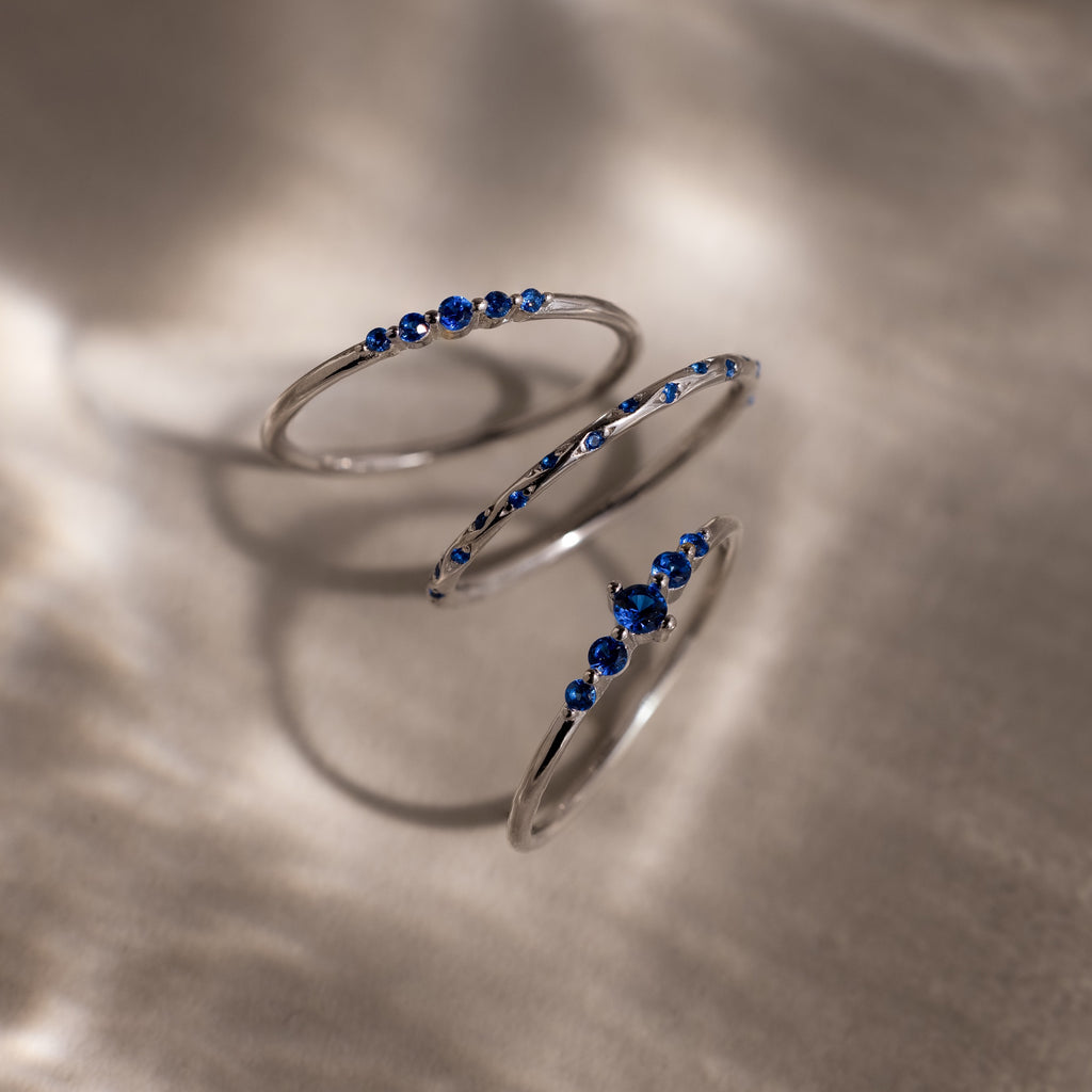 Three silver rings with blue gemstones on a textured surface