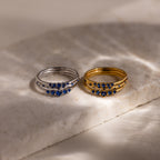 Two sets of 3 rings each, one set in silver and one set in gold, with blue stones on a marble surface.