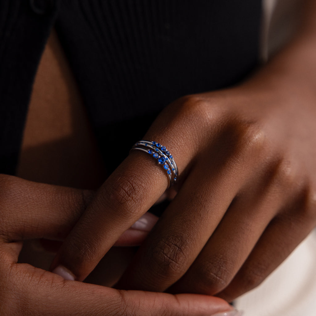 Close-up of a model wearing three silver stacking rings with blue gemstones.