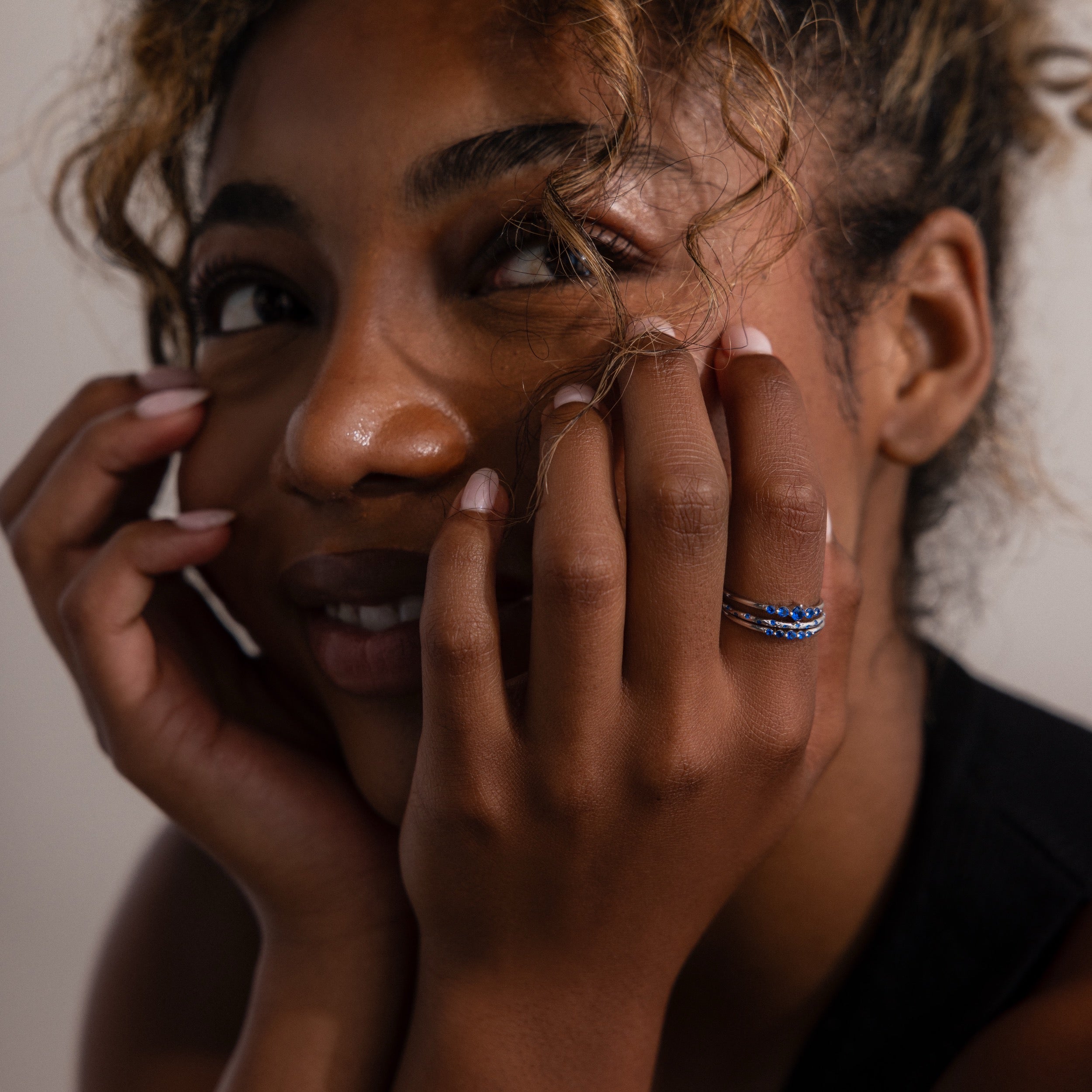 Woman with hands on face, wearing three silver stacking rings with blue gemstones.
