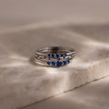 Stack of silver rings with blue sapphire stones on a marble surface