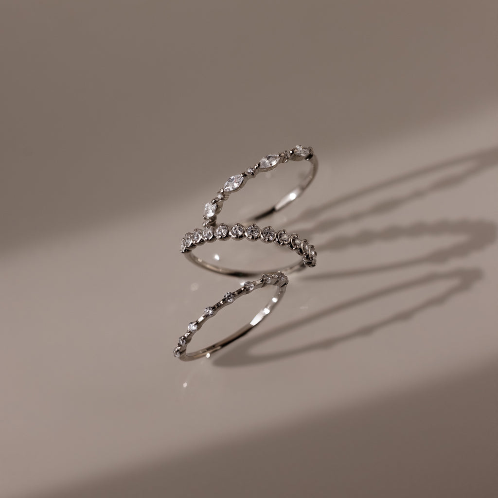 The Crystal Stacking Ring Set in Silver rests on a beige surface, each ring casting soft shadows as their gemstones sparkle delicately.