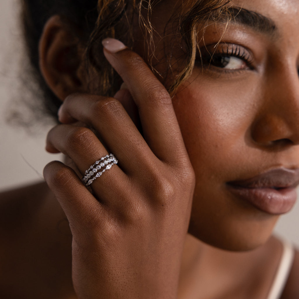 Elegant woman with curly hair showcases the Crystal Stacking Ring Set in Silver, adorned with sparkling gemstones, as she gazes softly at the camera.
