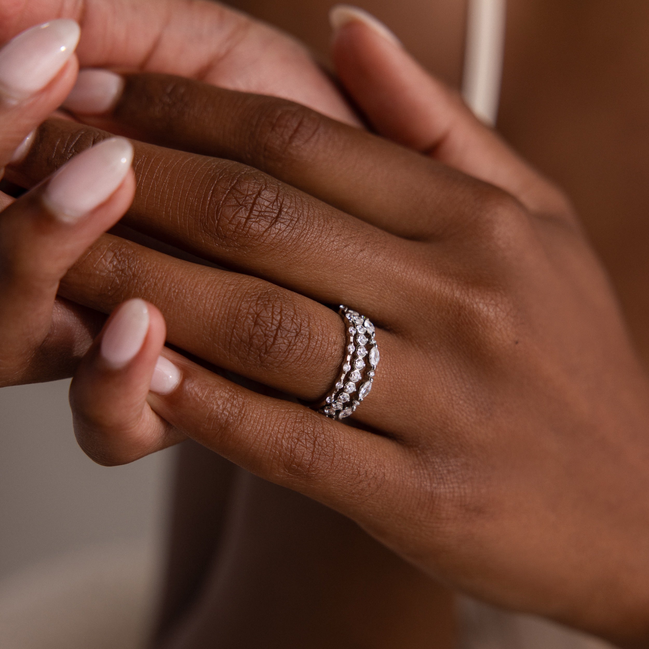 Close-up of a hand with manicured nails wearing the Crystal Stacking Ring Set in Silver, sparkling with crystal gemstones on the ring finger.