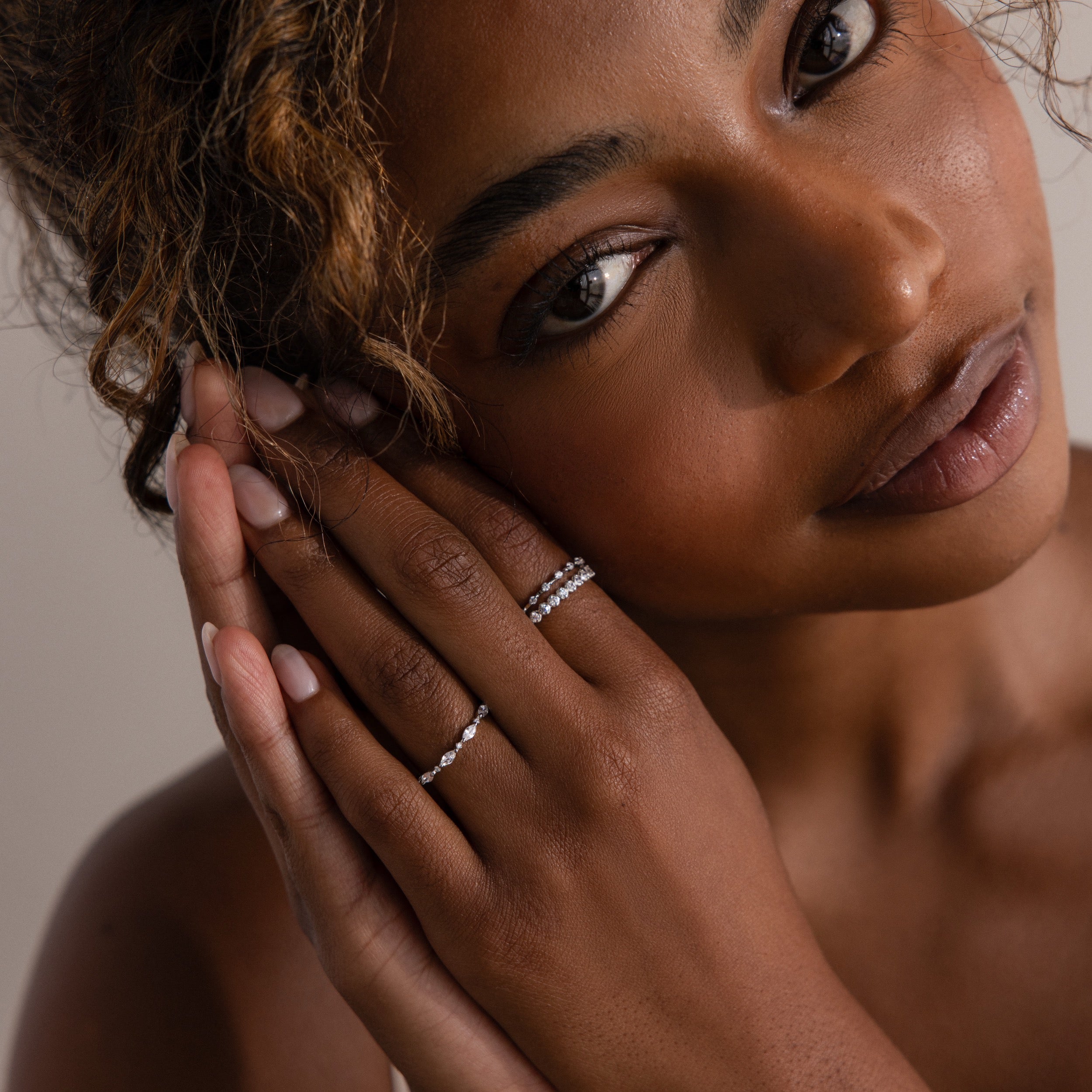 Woman with curly hair gazes softly, her hands near her face showcasing the elegant Crystal Stacking Ring Set in Silver adorned with crystal gemstones.