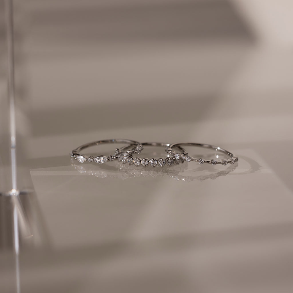 The Crystal Stacking Ring Set in Silver features three elegant rings with crystal gemstones, beautifully displayed on a smooth, reflective surface.