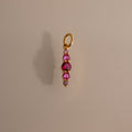 The Ombre Lace Ruby Charm is a gold pendant with four pink gemstones set vertically on a plain background.