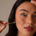 Smiling softly, a woman holds the Seaside Pearl Charm Bracelet in 18K Gold near her face—perfect for lovers of beachy jewelry and ocean-inspired charms.