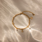The Seaside Pearl Charm Bracelet in 18K Gold features seashell, starfish, pearl, and heart ocean-inspired charms displayed on a softly lit neutral background.
