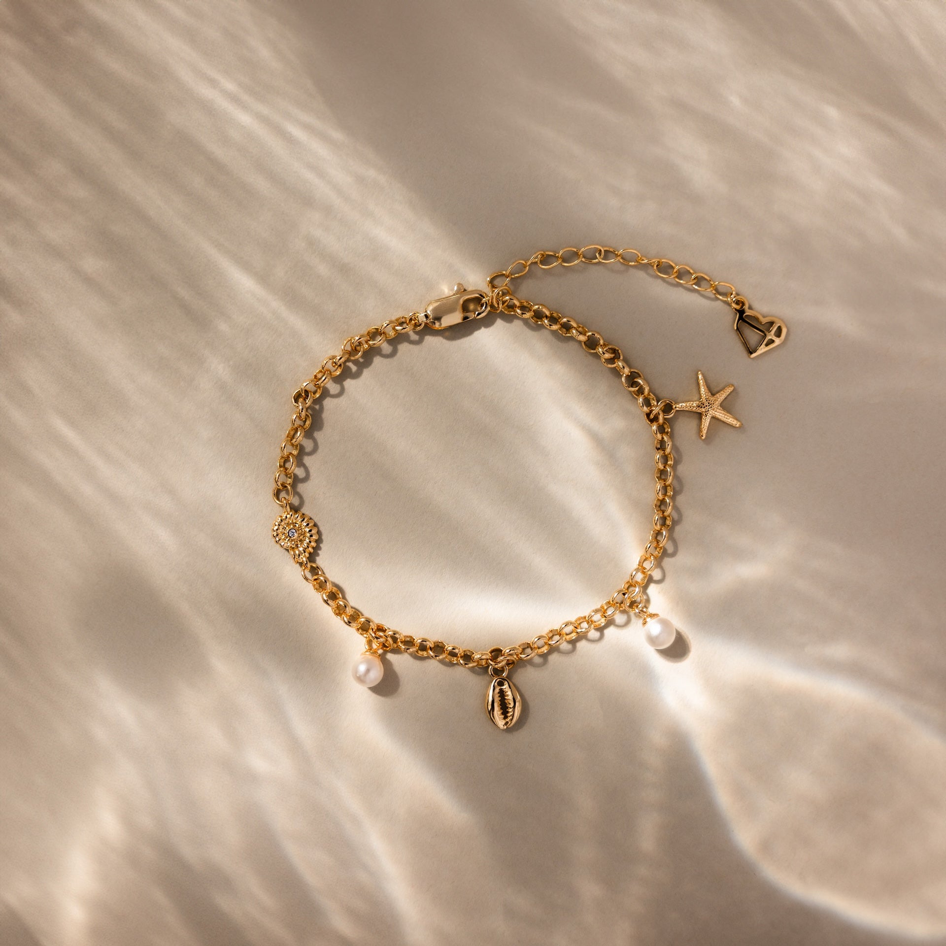 The Seaside Pearl Charm Bracelet shines on a sunlit, neutral background, featuring ocean-inspired charms—seashell, pearl, starfish, and heart. Ideal for anyone who loves coastal-themed jewelry.