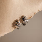 Celestial Sun Huggies in Silver, featuring a radiant sunburst design, are displayed on textured beige paper—perfect statement jewelry for any occasion.
