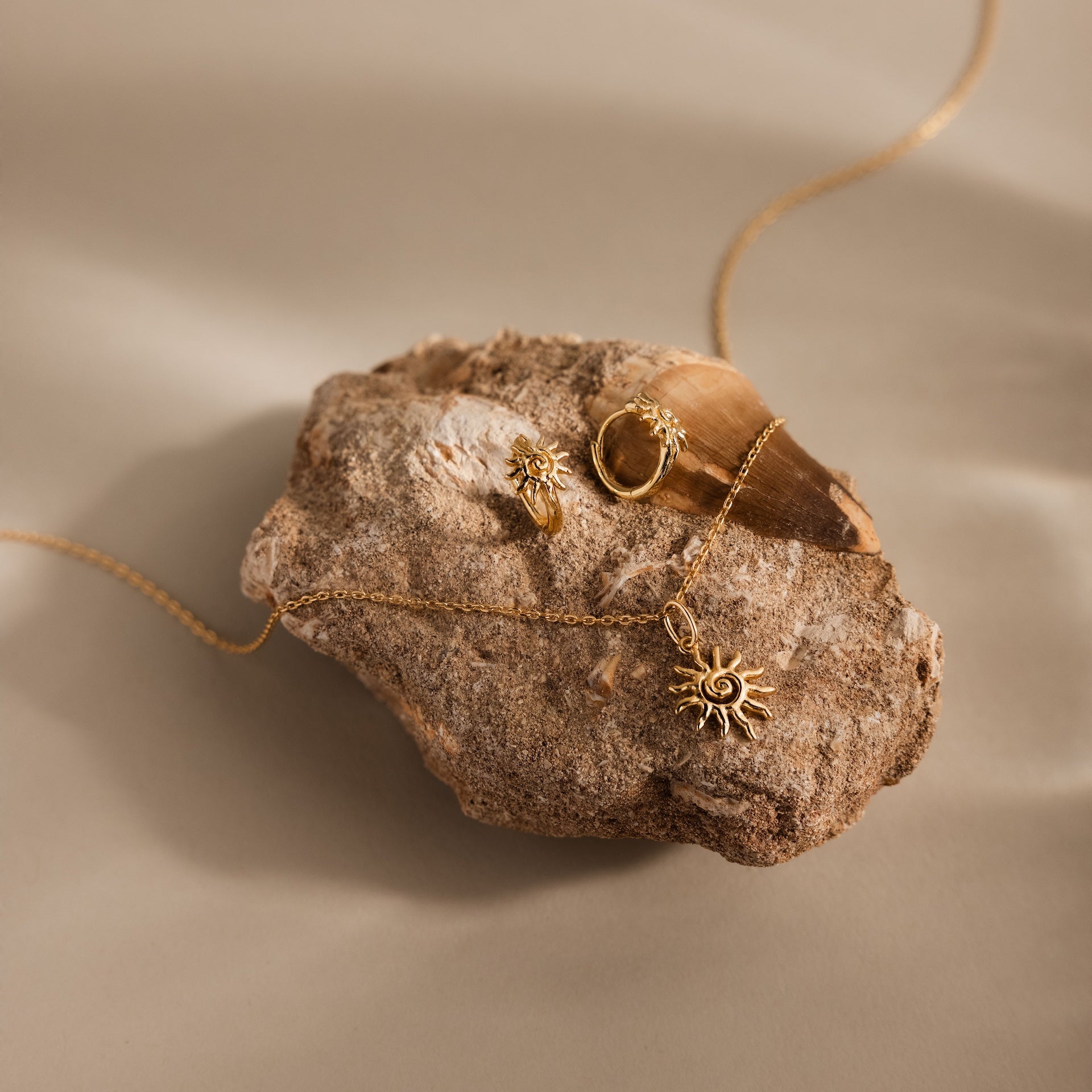 The Celestial Sun Huggies in 18K Gold are elegantly displayed on textured stone against a neutral background.