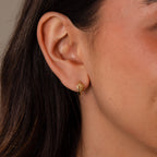 Close-up of a womans ear wearing Celestial Sun Huggies in 18K Gold—small sun-shaped earrings with dangling detail, perfect for adding a touch of statement jewelry.