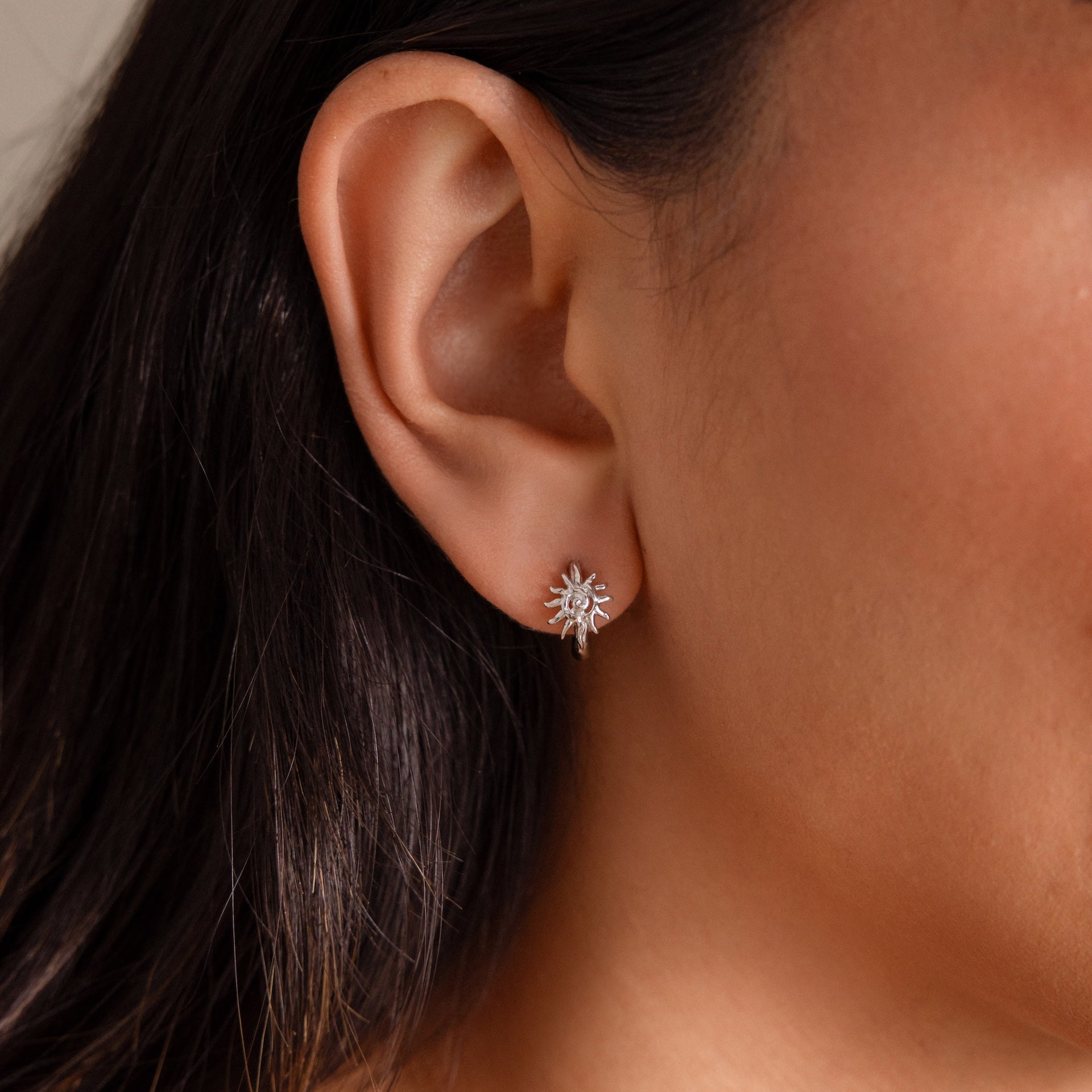 Close-up of a womans ear wearing Celestial Sun Huggies in Silver—dainty sunburst earrings with clear gemstones, perfect for a subtle statement.